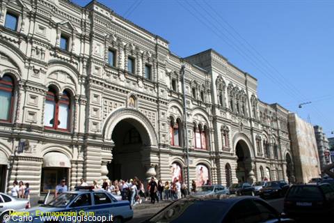White stone facade of GUM department store, tourists and cars under blue sky