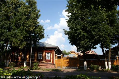 Carved wooden house in Suzdal, golden gates among tall trees