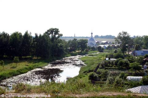 Suzdal: river with water lilies, white church with blue domes among trees and houses