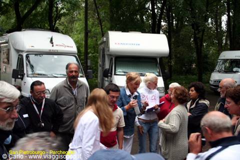 Group of campers gathered among motorhomes and trees in green area