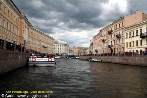 Tour boat on canal between pastel buildings in Saint Petersburg, cloudy sky