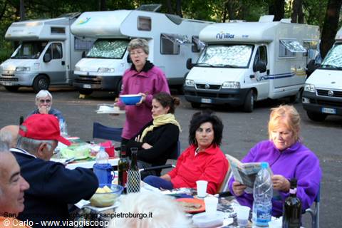 Campers having lunch among parked motorhomes, a woman serving bowls