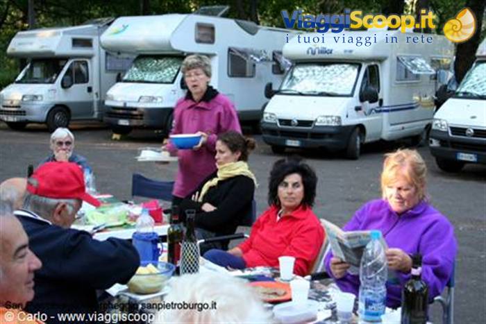 Campers having lunch among parked motorhomes, a woman serving bowls