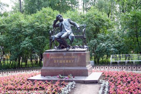 Bronze statue of seated Pushkin on a bench, among pink flowers and green trees