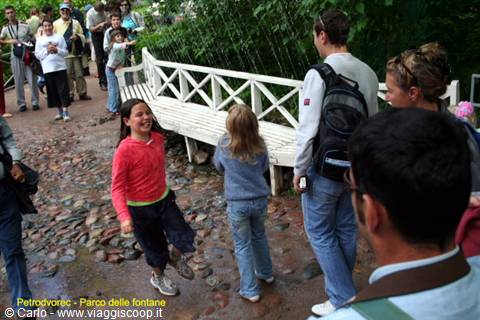 Tourists and children on wet gravel beside a white wooden bench, Petrodvorets