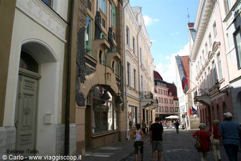 Pedestrians walk on cobblestones in a Tallinn street with colorful facades