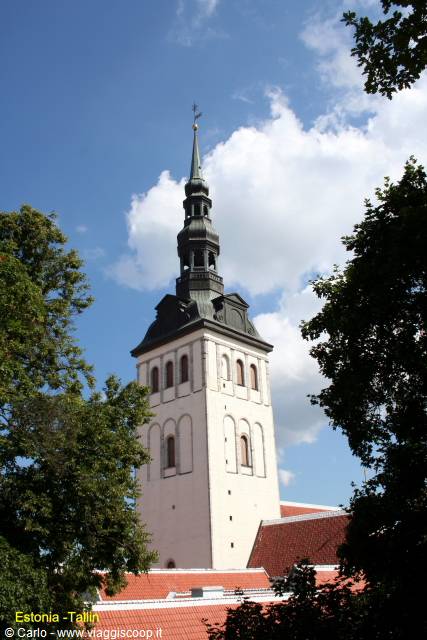 White Gothic tower of St. Nicholas Church, Tallinn, framed by trees