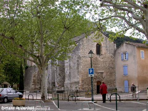 Romanesque stone church in Fontaine-de-Vaucluse, plane trees and people in square