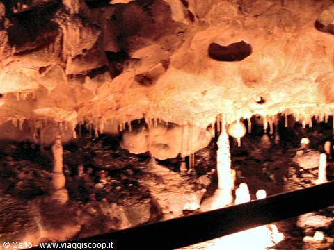 Stalactites and stalagmites inside a cave, warm artificial light on rock