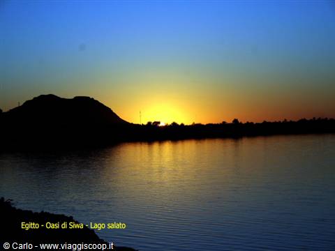 Sunrise over Siwa salt lake, dark hill on the left, orange sky and calm waters