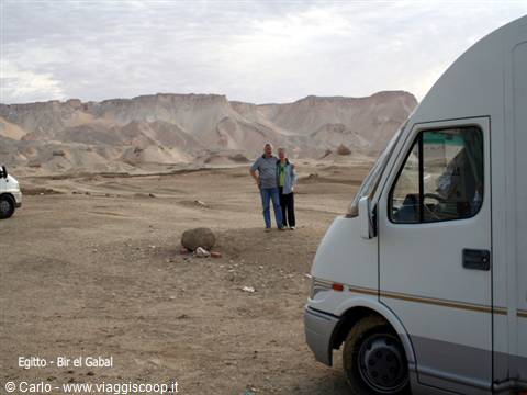 Couple standing beside their camper van near rocky desert mountains at Bir el Gabal