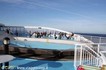 Passengers seated around the empty pool on the ship deck