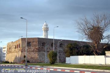 Old stone walls with white lighthouse, palm trees and morning street