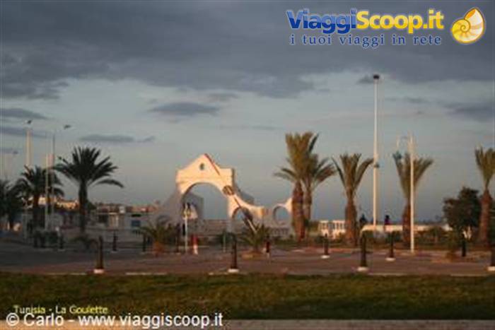 White arch and palm trees in a square at sunset