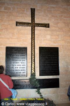 Metal cross above black plaques honoring the 1939-1945 fallen, stone wall