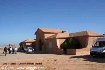 Brick entrance of Tobruk War Cemetery, visitors and campervan under blue sky