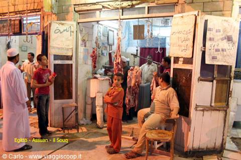 Butcher shop in Aswan souq, hanging carcasses and men waiting under neon lights