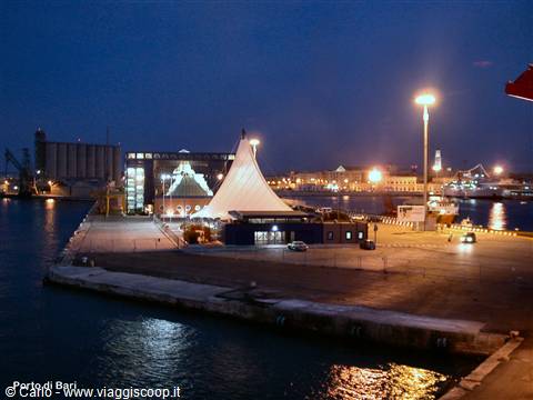 Bari harbor at night: illuminated white tent tent on the pier, lights reflecting on water