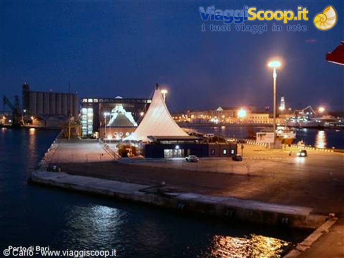Bari harbor at night: illuminated white tent tent on the pier, lights reflecting on water