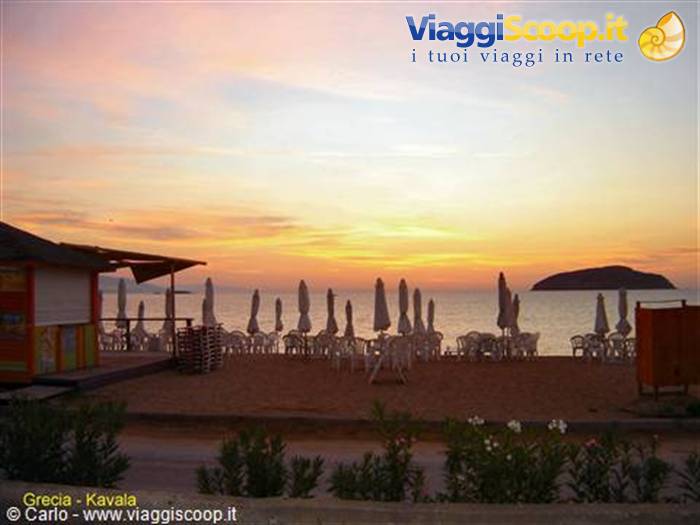 Kavala beach with closed umbrellas and an island on the sea at sunset