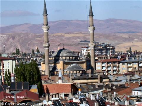 Mosque with dome and two minarets above Sivas rooftops, arid hills behind