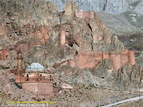 Mosque with minaret and dome beneath red fortress walls carved into the cliff