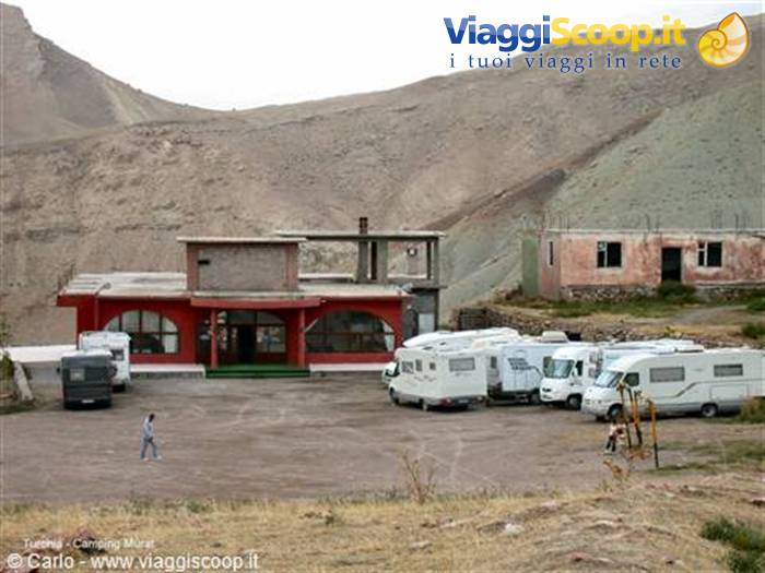 Motorhomes parked at Camping Murur, red building among arid hills