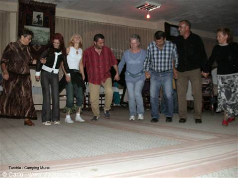 Tourists dancing hand in hand indoors at Camping Murat, warm light