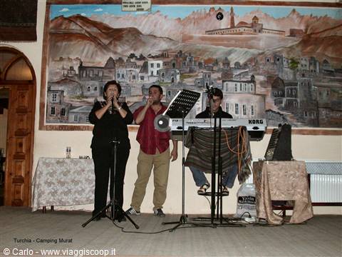 Musicians singing and playing a Korg keyboard in front of a town mural