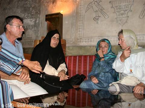 Visitors seated on sofas inside Shiraz's old Vakil bathhouse, murals behind