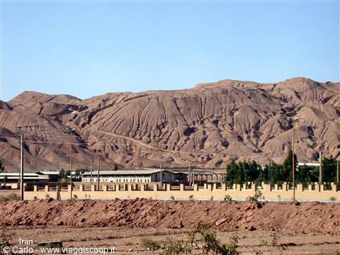 Eroded barren mountains above low buildings and green trees under blue sky
