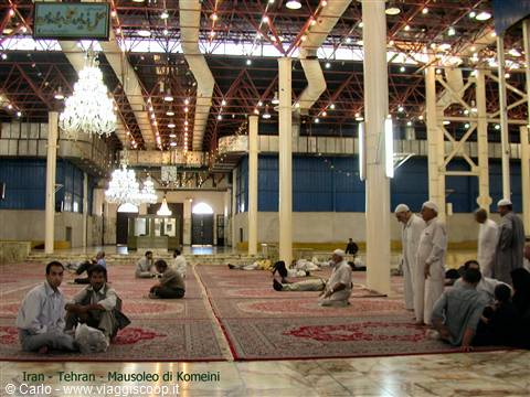 Pilgrims resting on carpets inside Khomeini's Tehran shrine, chandeliers and steel trusses