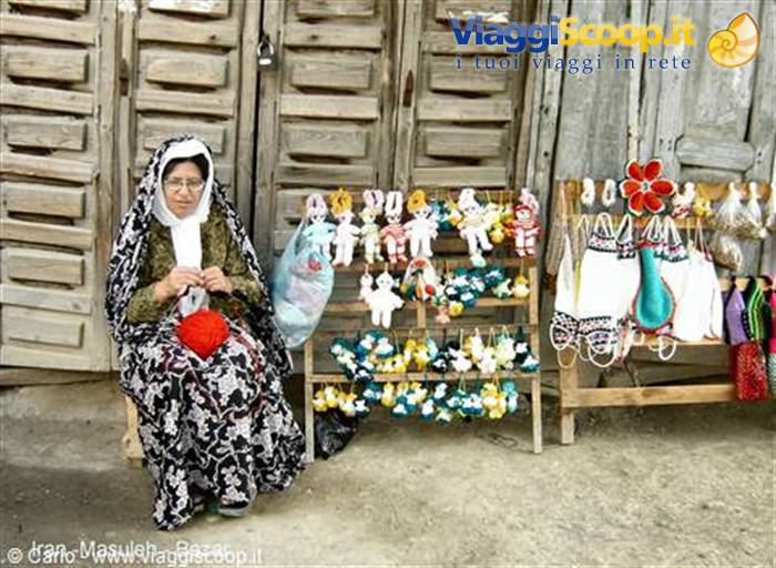 Veiled craftswoman knits wool dolls before wooden doors in Masuleh