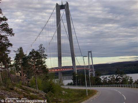 Högakustenbron suspension bridge among pines, curving road under cloudy sky