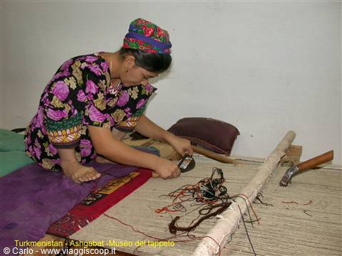 Woman in floral dress weaves a carpet on a loom at Ashgabat museum