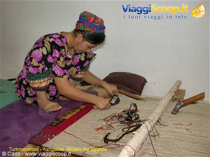 Woman in floral dress weaves a carpet on a loom at Ashgabat museum