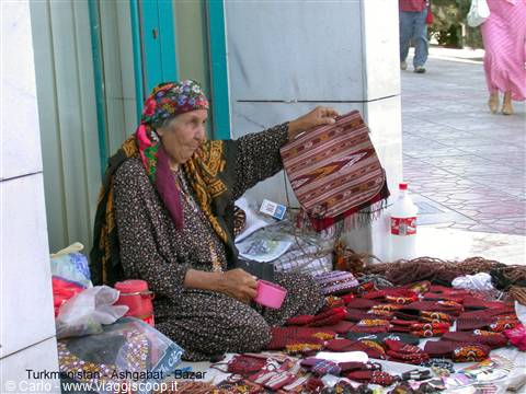 Ashgabat bazaar: elderly vendor shows handmade woven bags on the ground