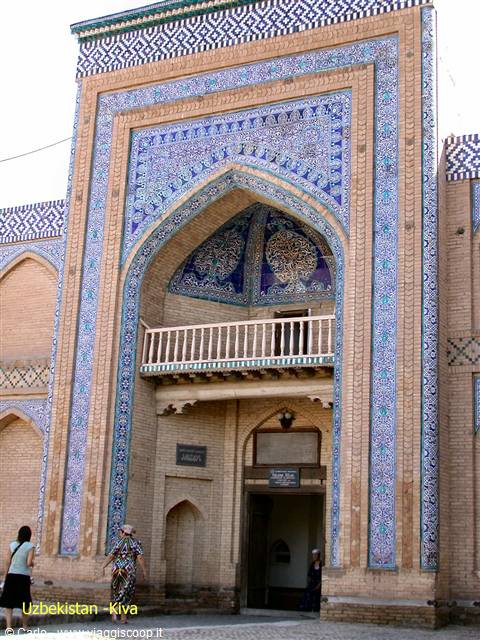 Brick portal with blue tiles at a madrasa entrance, visitors beneath the iwan in Khiva
