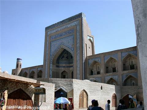 Brick madrasa with blue-tiled portal in Khiva, tourists under the sun
