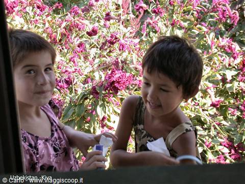 Smiling children at a window among pink flowers in Khiva