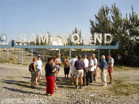 Tourists gathered under the large metal Samarkand sign on a sunny day