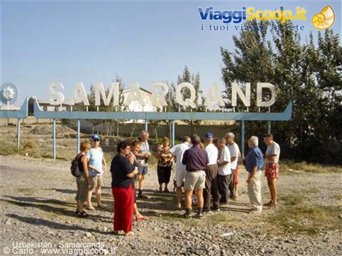 Tourists gathered under the large metal Samarkand sign on a sunny day