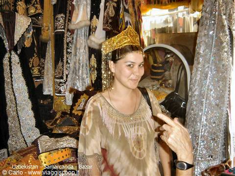 Woman wearing golden headdress at Samarkand bazaar among embroidered robes