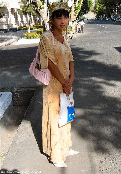 Woman in golden dress and traditional headdress on a Tashkent sidewalk
