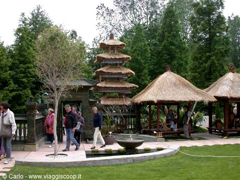 Visitors walk past a thatched pagoda and gazebo in a garden