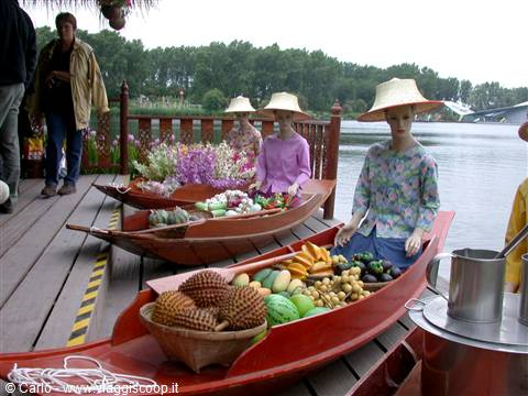 Red wooden boats with exotic fruit and mannequins in straw hats by the lake