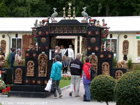 Visitors walk through a large carved wooden gate with deities and tridents