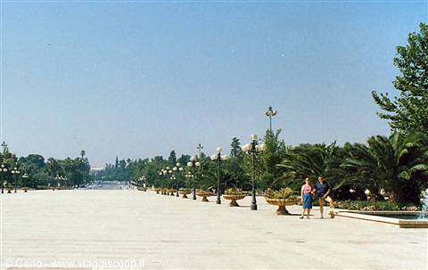 Coppia che cammina su un largo piazzale alberato con palme e lampione