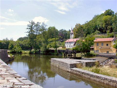 Stone weir and sluice on a river, yellow houses and church spire among trees