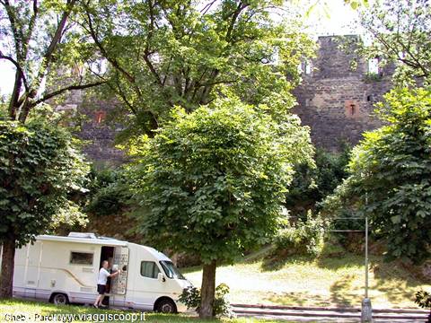 White camper van parked among trees, old castle walls behind